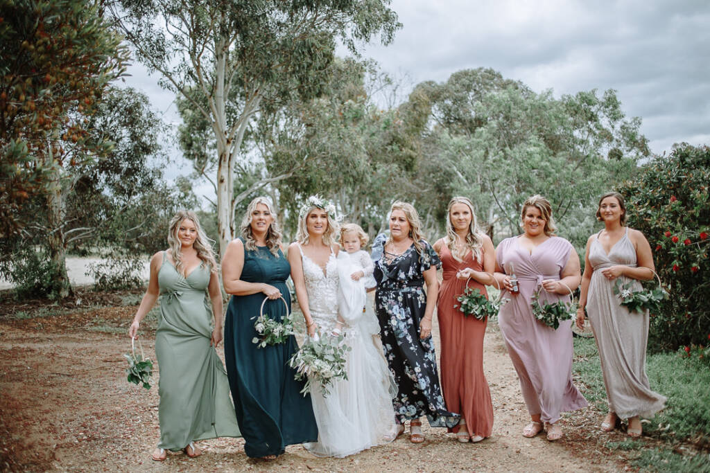 Kelly and a child pose with the wedding party on the gravel drive at Camp Sunnystones.