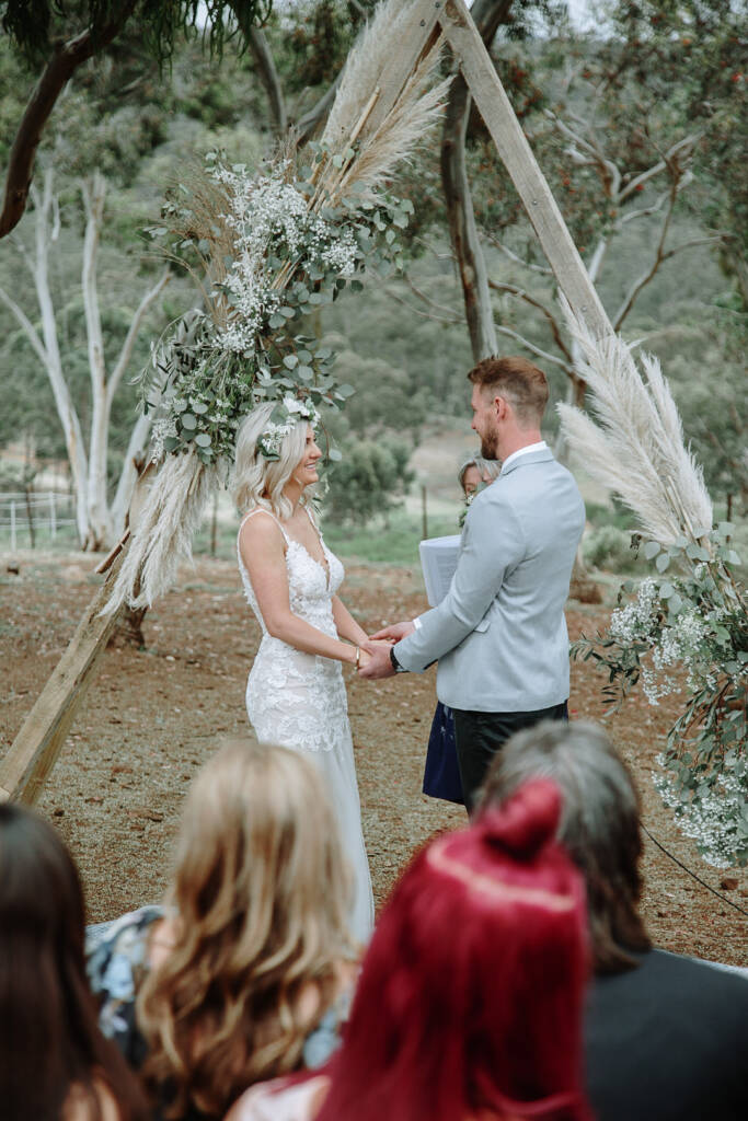 Kelly and Tory hold hands beneath the timber arbour during their bush ceremony at Camp Sunnystones.