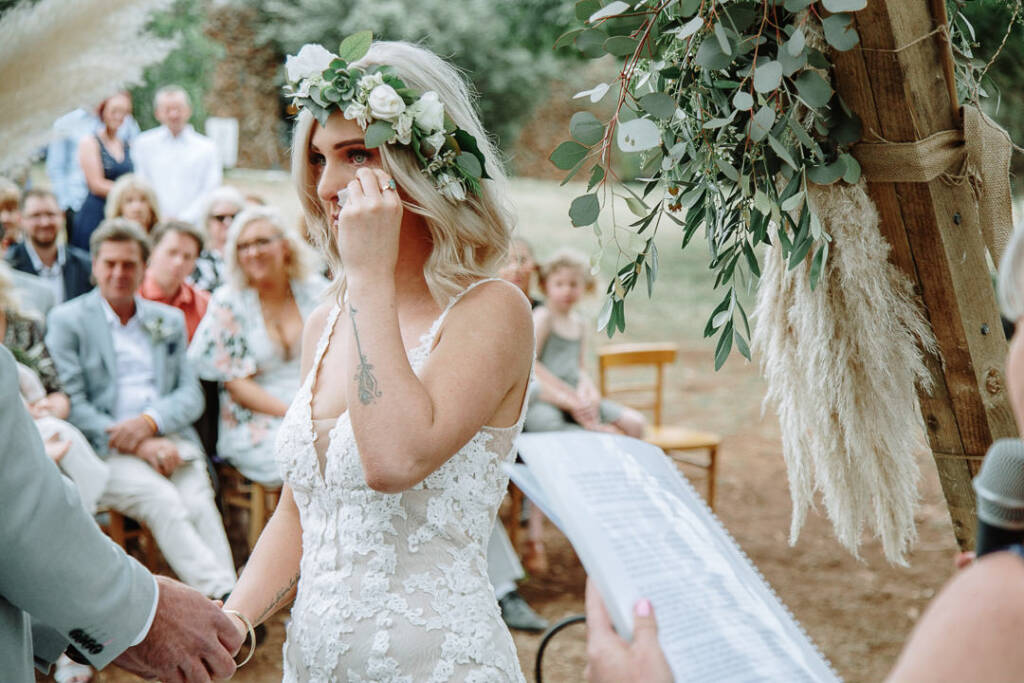 Kelly dabs her eye while holding Tory’s hand beneath her flower crown.