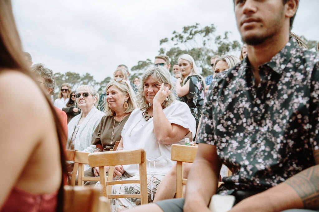 A seated wedding guest touches her eye while watching the ceremony.