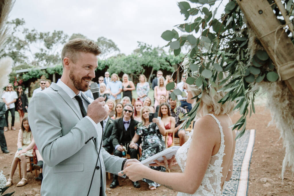 Tory smiles into a microphone while holding Kelly’s hand during the ceremony.