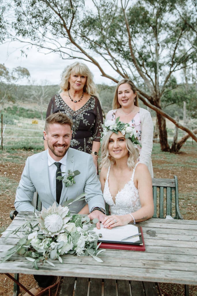 Kelly and Tory pose at the signing table with the celebrant and a witness at Camp Sunnystones.