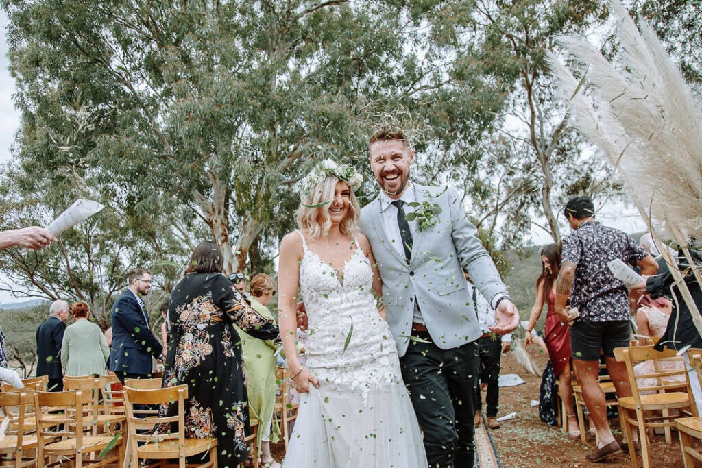 Leaf confetti falls around Kelly and Tory as they leave their country wedding ceremony at Camp Sunnystones.