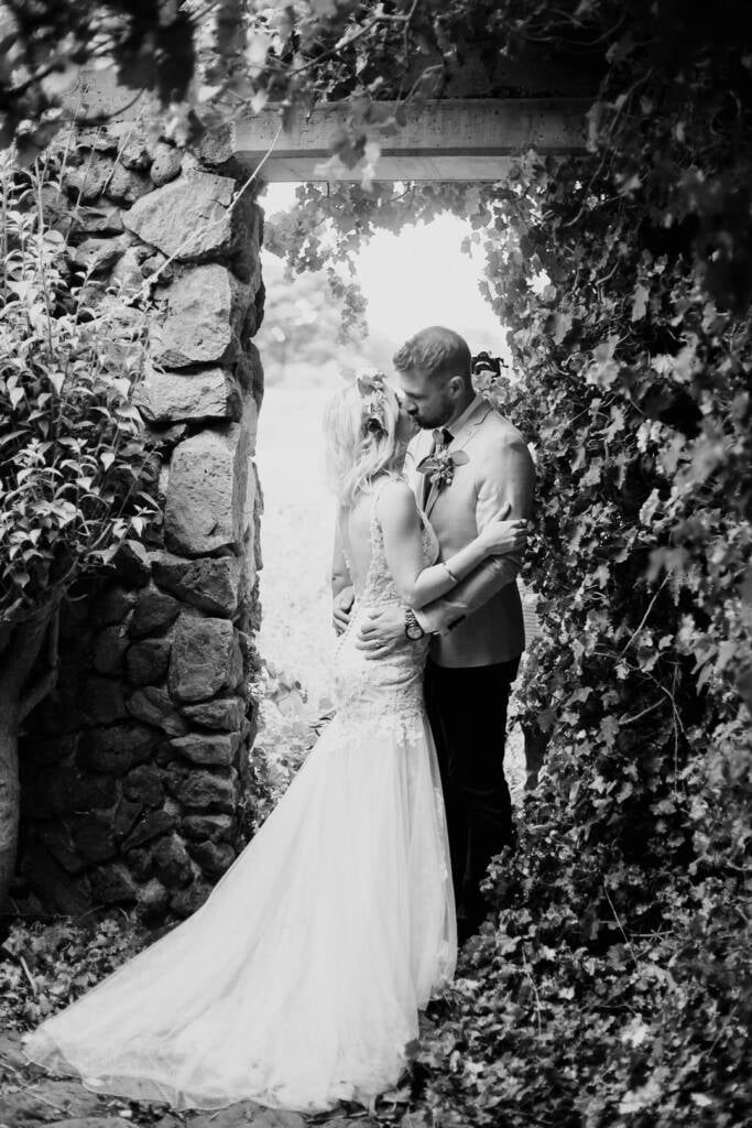 Black-and-white portrait of Kelly and Tory kissing in Sunnystones’ vine-covered stone doorway.