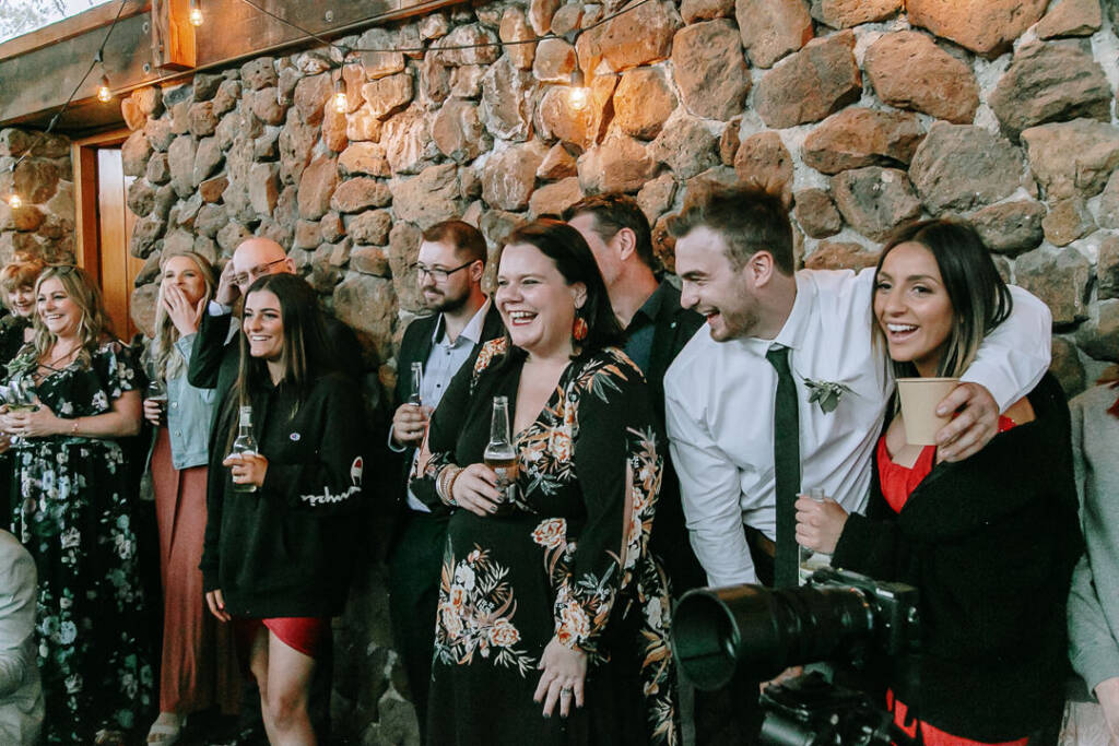 Guests laugh with drinks beside the stone wall at Camp Sunnystones.