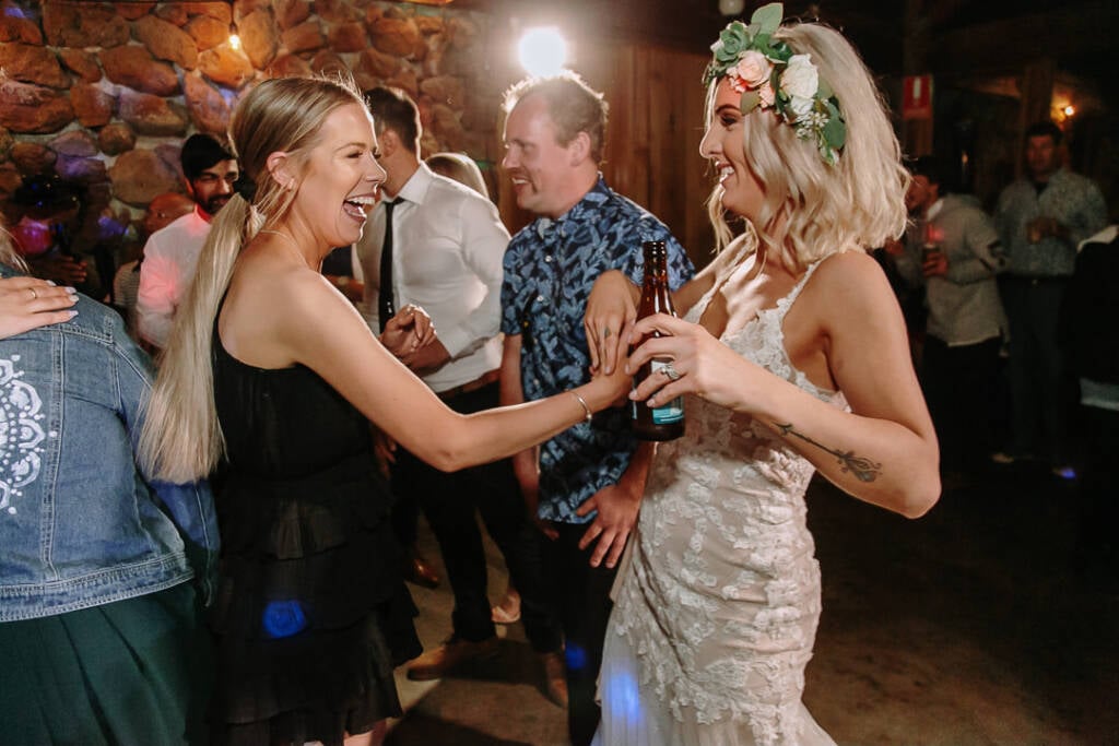 Kelly laughs and dances beside a guest in a black dress holding a beer bottle.