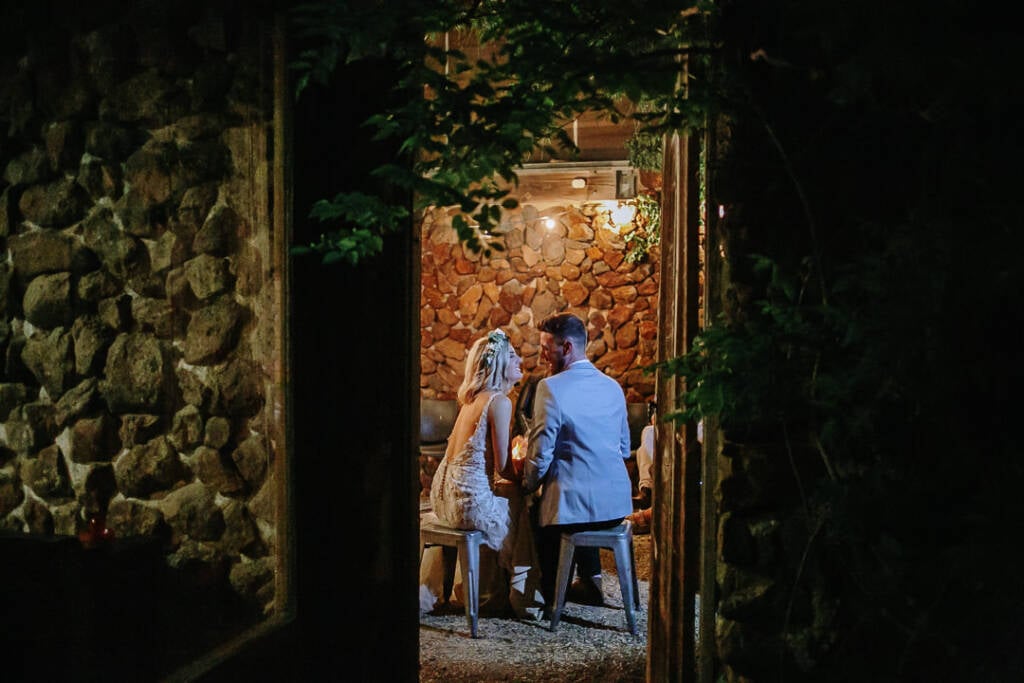 Kelly and Tory have a night photo taken seated inside Camp Sunnystones, framed by a dark leafy doorway.