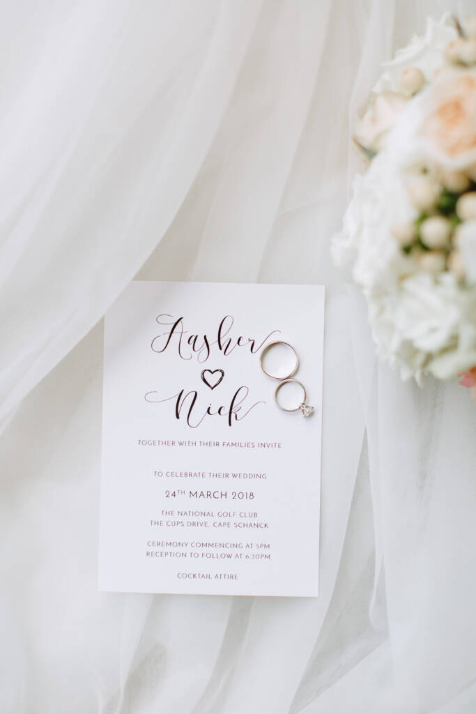 Invitation flat lay on tulle for Aasher and Nick, two rings resting on the lettered card.