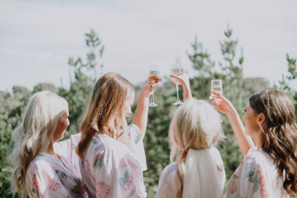 Aasher and three bridesmaids raise champagne flutes against pine trees at their Cape Schanck Airbnb.