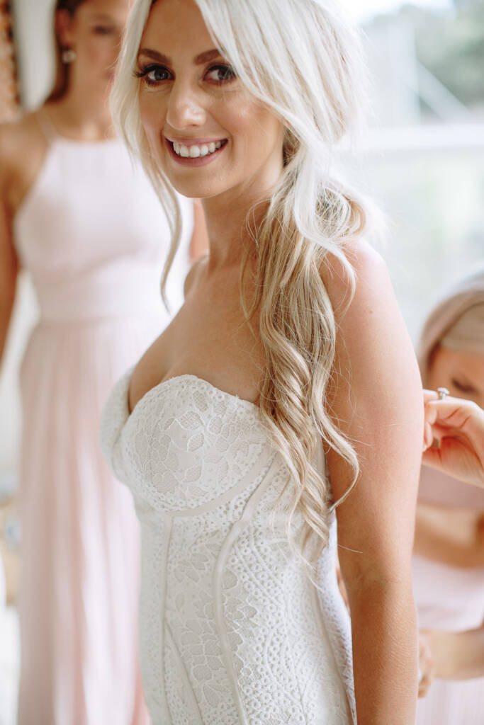 Aasher smiles at the camera in the lace bodice while a bridesmaid works at her back.