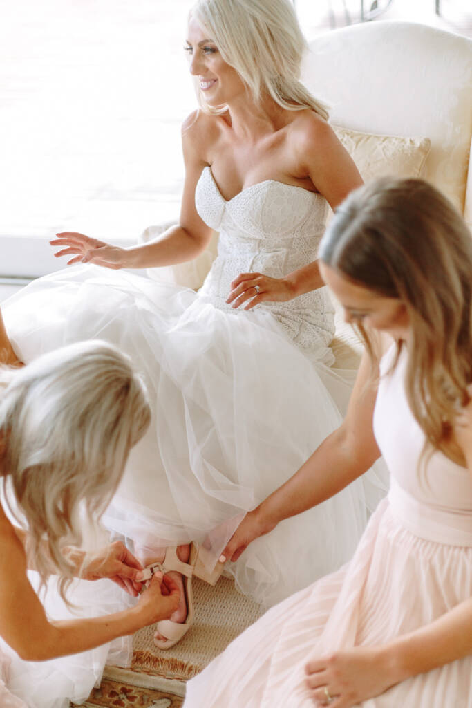 Laughing in the wingback chair, Aasher has a blush heeled sandal buckled beneath the tulle.