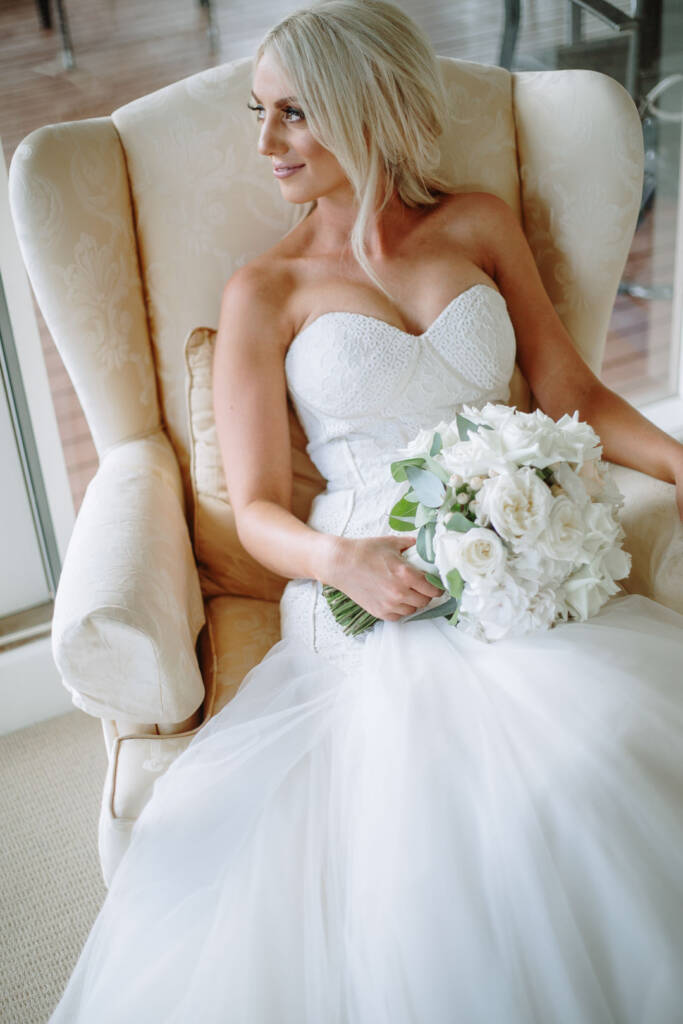 Seated bridal portrait of Aasher with a white rose and peony bouquet, tulle skirt spread wide.