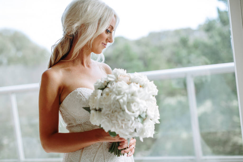 Profile of Aasher at the window looking down at her white rose and peony bouquet.