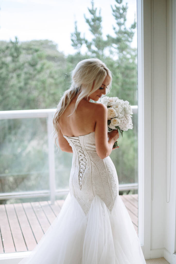 Ribbon lacing and tulle flare from behind as Aasher glances down at her bouquet over her shoulder.