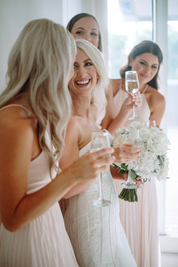 Aasher laughs at the centre of her bridesmaids as they raise their flutes by a bright window.