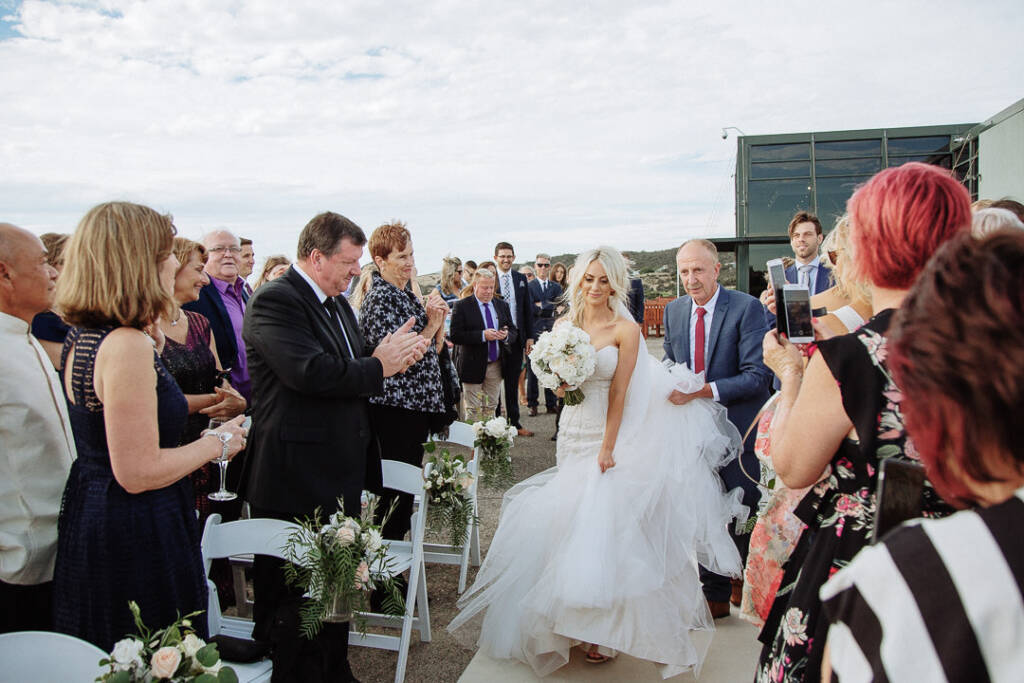 Aasher and her escort walk down the aisle at The National Golf Club as guests stand and applaud.