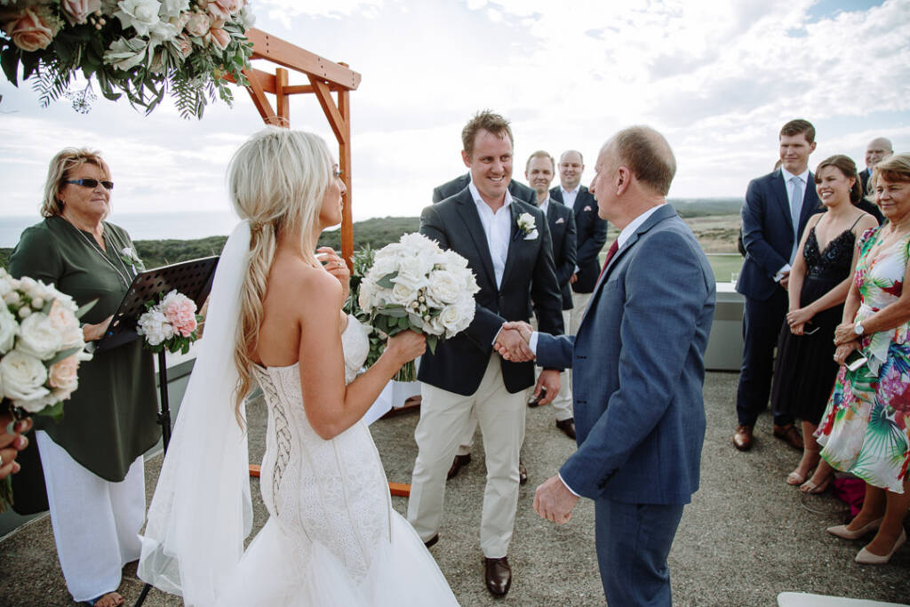 Nick shakes the escort's hand beneath The National's floral ceremony arbour, with the ocean beyond.