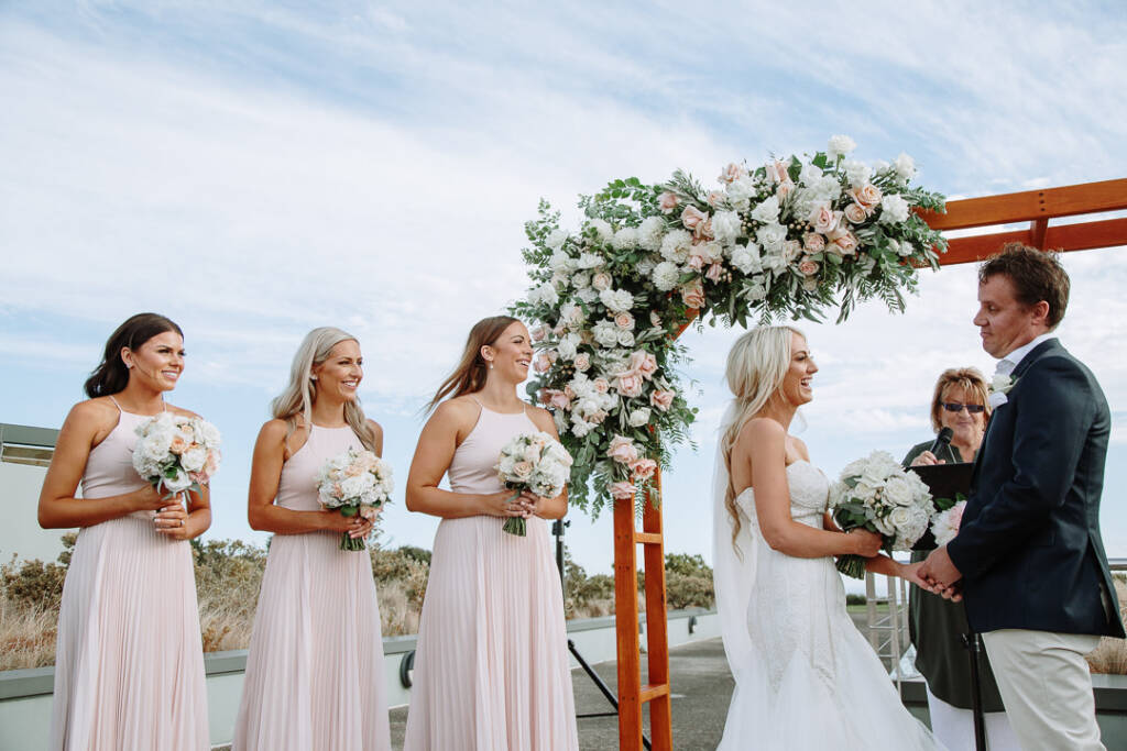 Aasher and Nick hold hands beneath The National's floral arbour as bridesmaids laugh.