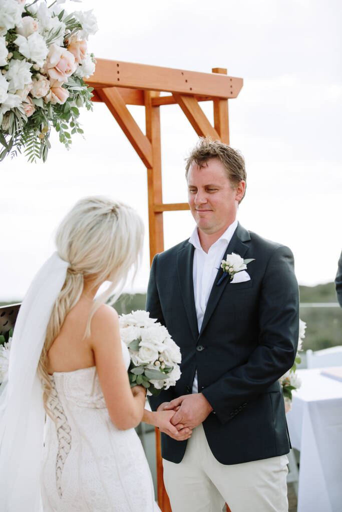 Nick smiles at Aasher and holds her hands beneath the ceremony arbour at The National.