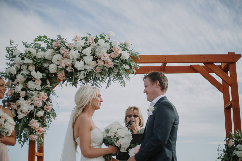 Aasher and Nick face one another as the celebrant speaks beneath The National's floral arbour.