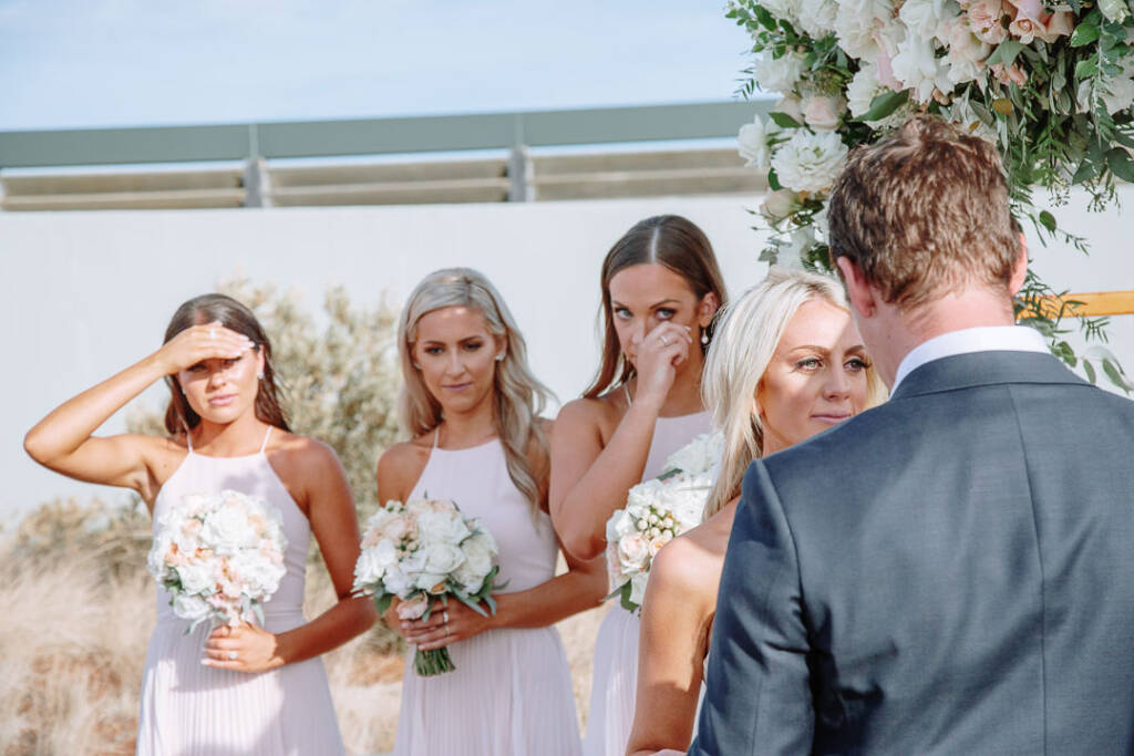Three bridesmaids listen to the vows at The National Golf Club; one shades her eyes from the sun.