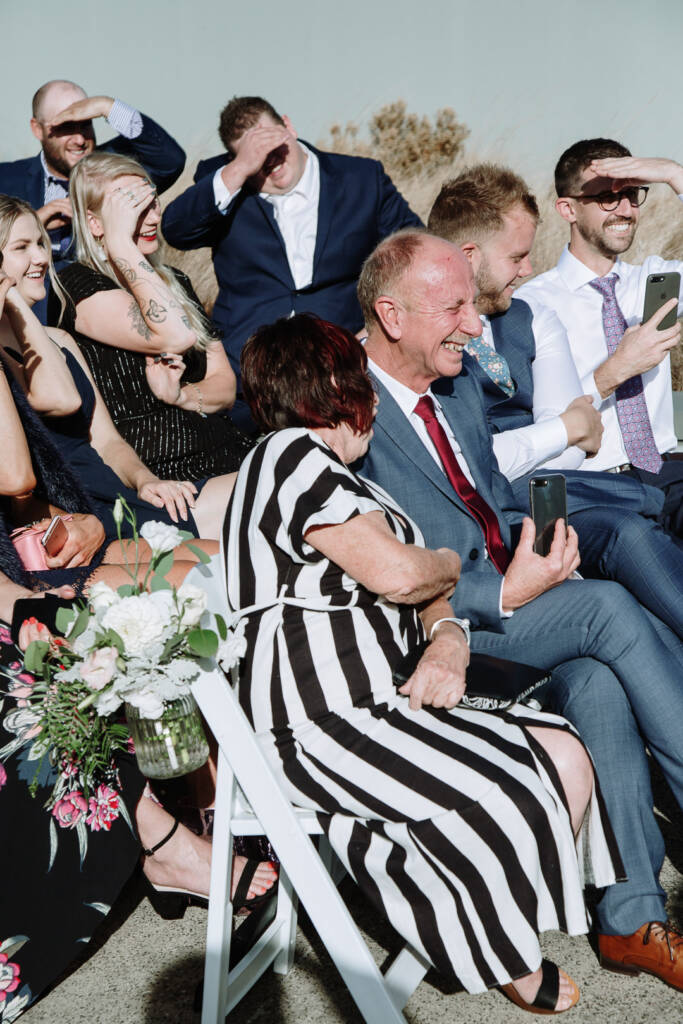 Seated guests laugh and shade their eyes from the sun during The National Golf Club's outdoor ceremony.