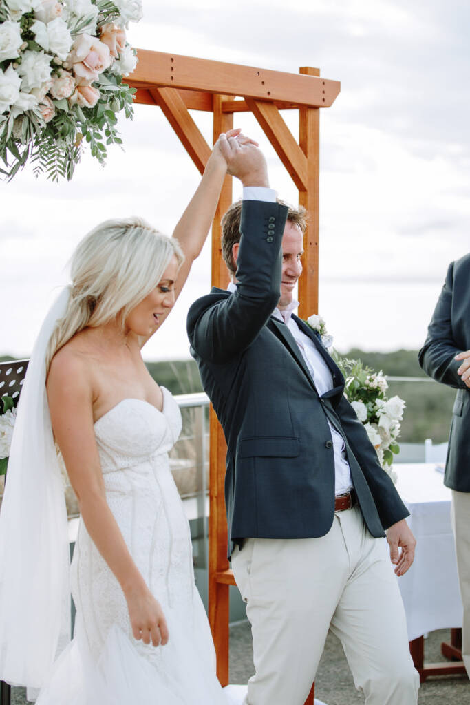 Nick raises Aasher's hand beneath The National's ceremony arbour, with the ocean beyond the balustrade.