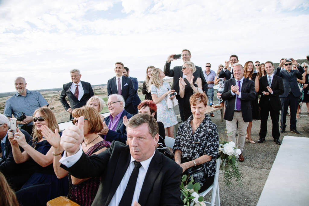 Guests applaud and film the moment, one man at the front giving a thumbs up.
