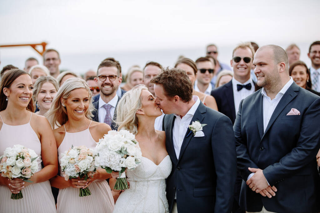 Aasher and Nick kiss amid guests on The National's terrace beneath a bright sky.