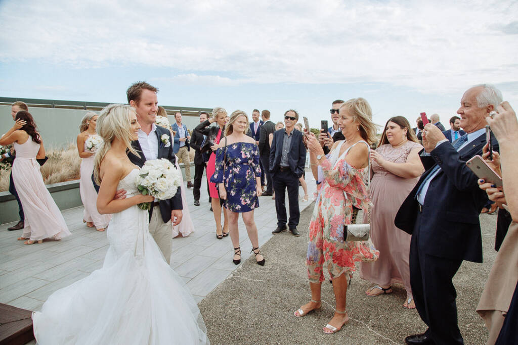 Guests raise their phones to photograph Aasher and Nick, bridesmaids gathered behind them.