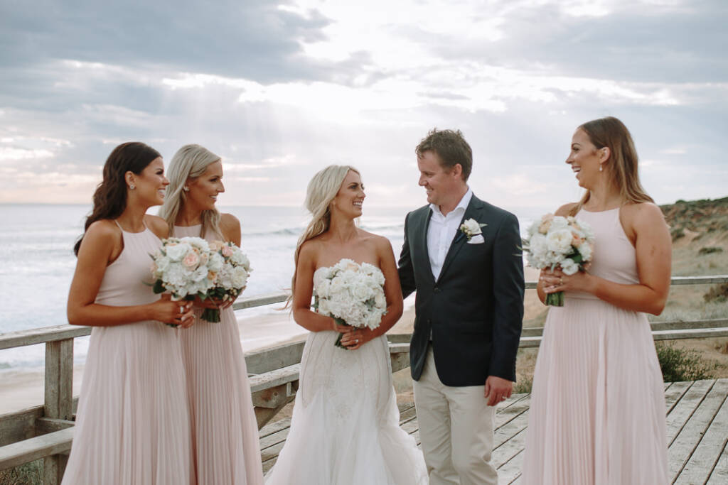 Aasher and Nick laugh with three bridesmaids on the boardwalk above Fingal Beach.