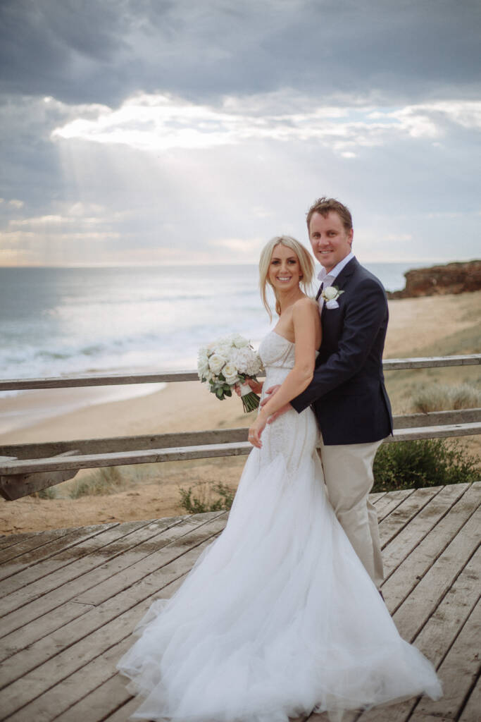 Nick embraces Aasher above Fingal Beach as sun rays break through clouds over the surf.