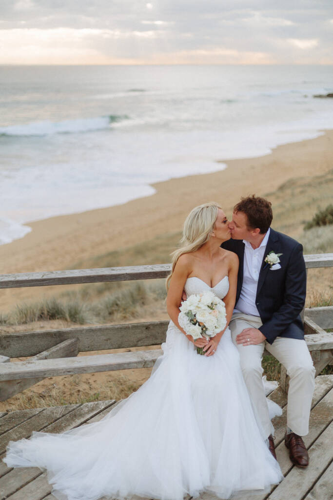 Aasher and Nick kiss while seated on the timber lookout above Fingal Beach.