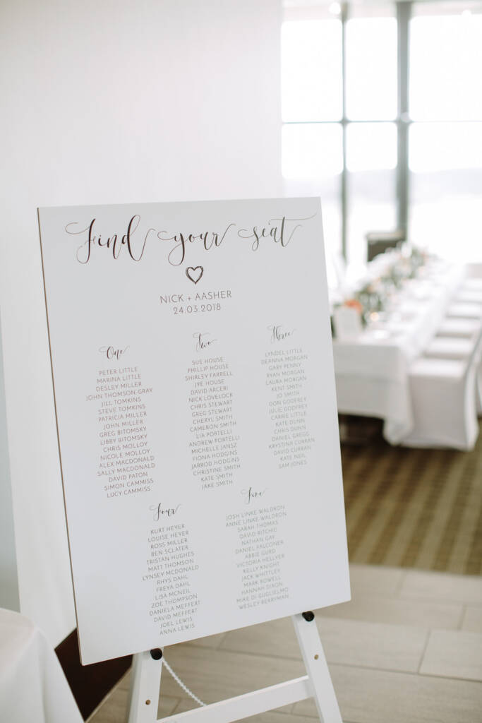 A find-your-seat board for Aasher and Nick stands before long tables at The National Golf Club.