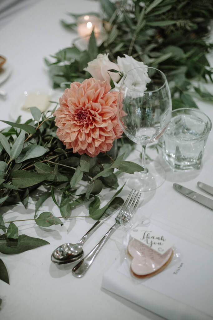Heart-shaped biscuit favour beside white roses and eucalyptus on a National Golf Club reception table.