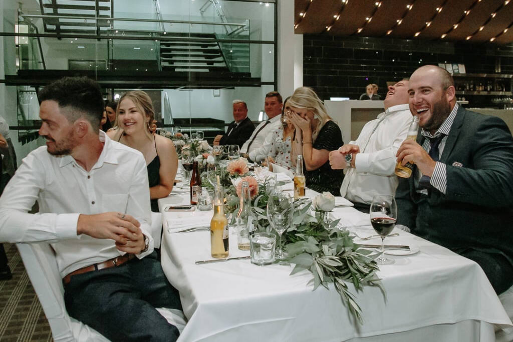 Guests laugh at a long table during a speech at The National Golf Club.