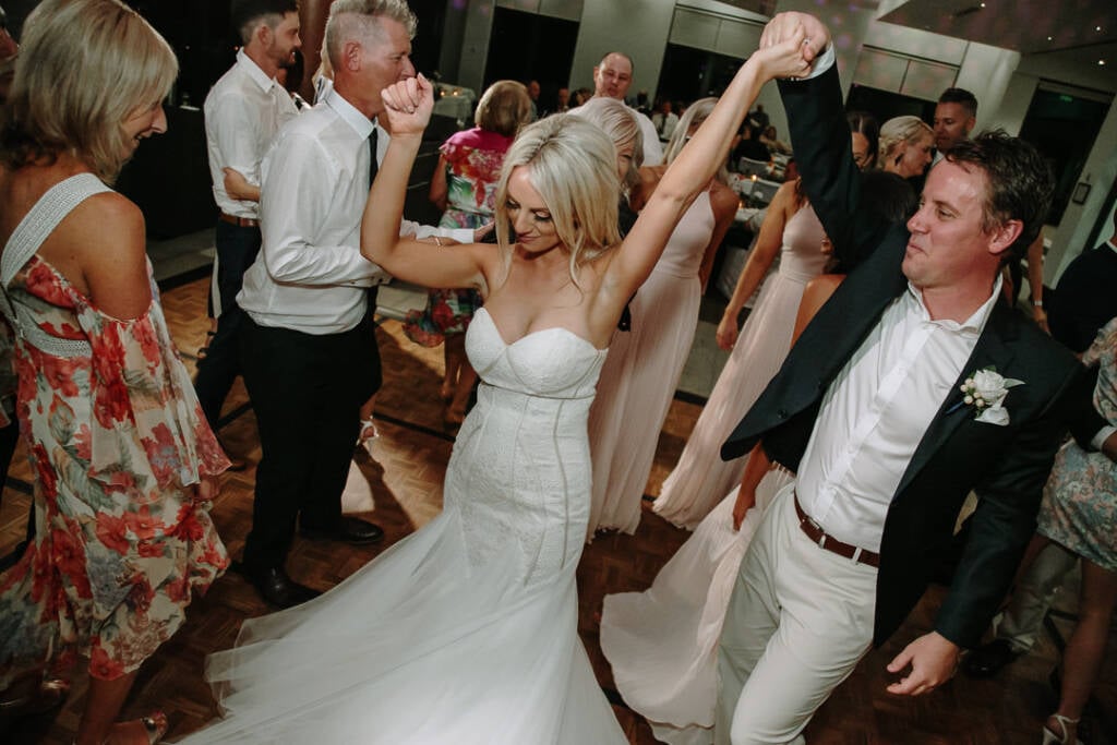 Nick holds Aasher's hand high as she dances, bridesmaids in blush and guests around them.
