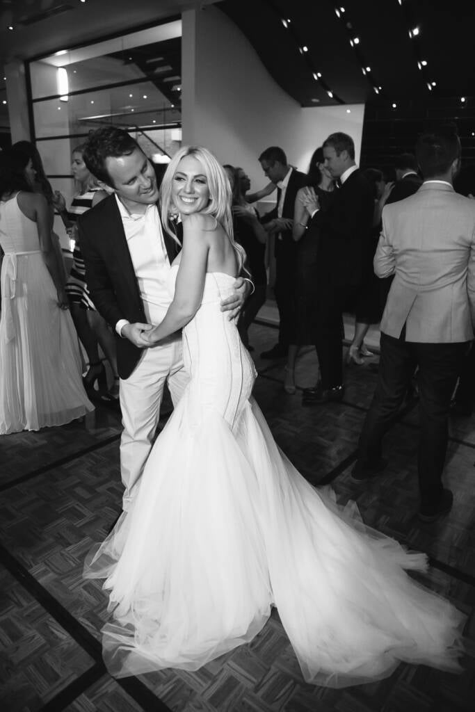 Nick holds Aasher from behind on The National's dance floor as they smile at the camera.