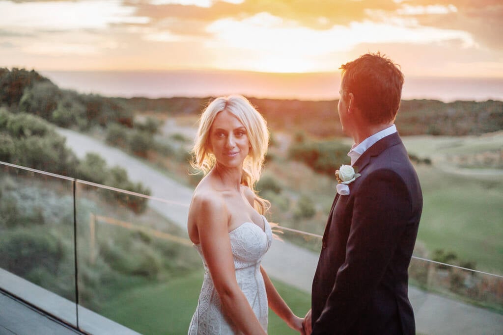 Aasher looks back at the camera beside Nick on The National's terrace, with sunset over the fairway.