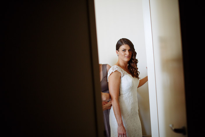 Pascale looks towards the camera as another woman helps with the back of her lace gown.