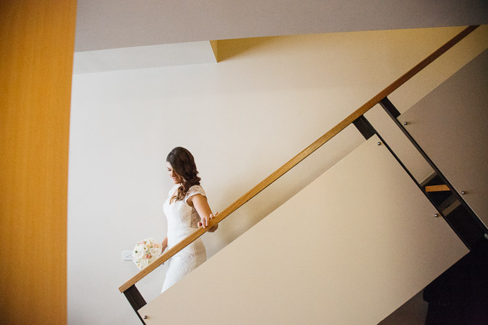 Pascale descends the stairs at Quest on William with her bouquet and one hand on the rail.