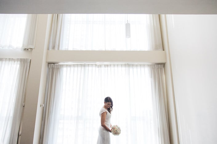 Tiny beneath the double height windows at Quest on William, the bride checks her bouquet.