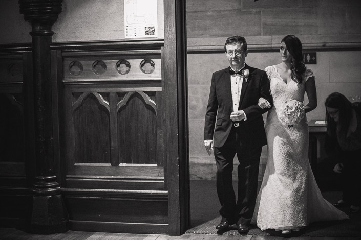The bride enters Chapter House arm-in-arm with a man in a bow tie.