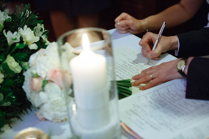 A hand signs a document beside flowers and a candle at The Chapter House.