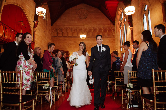 Pascale and Pasquale walk down the red-carpeted aisle at Chapter House as guests stand beside them.