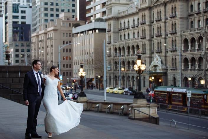 The bride's skirt fans on the Parliament House steps, the Windsor lit across the road.