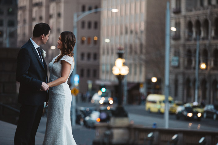Pascale and Pasquale hold hands on the Parliament House of Victoria steps, with city lights behind.