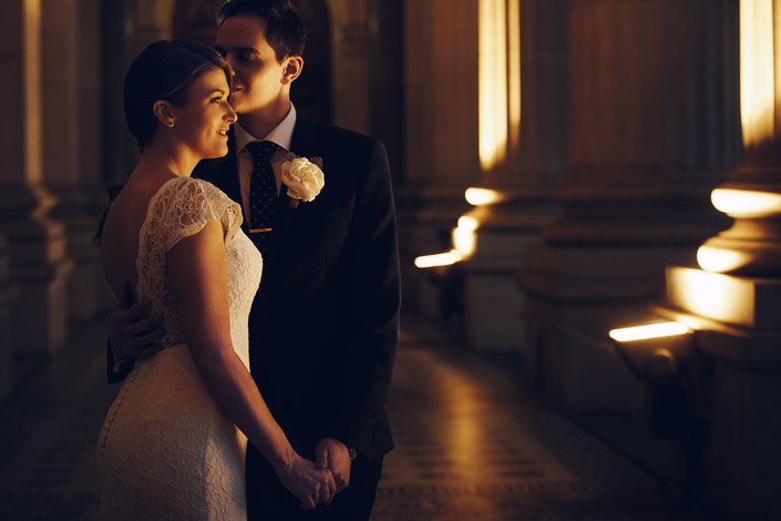 Pascale and Pasquale hold hands beside the warmly lit columns of Victorian Parliament House.