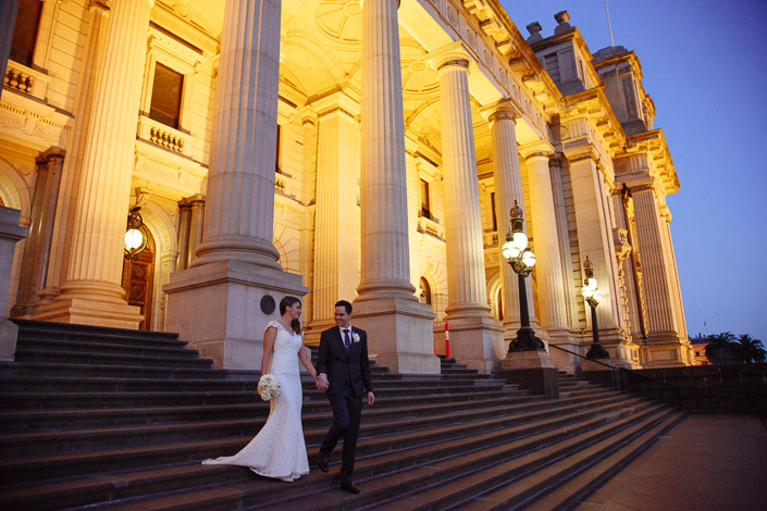 Pascale and Pasquale descend the illuminated Parliament House steps in Melbourne CBD at blue hour.