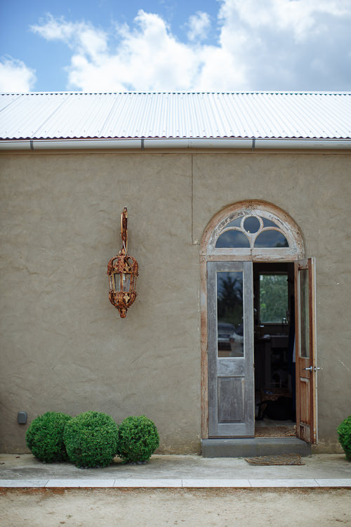 An arched timber door with a fanlight stands open in a rendered wall beside a rusted iron lantern.